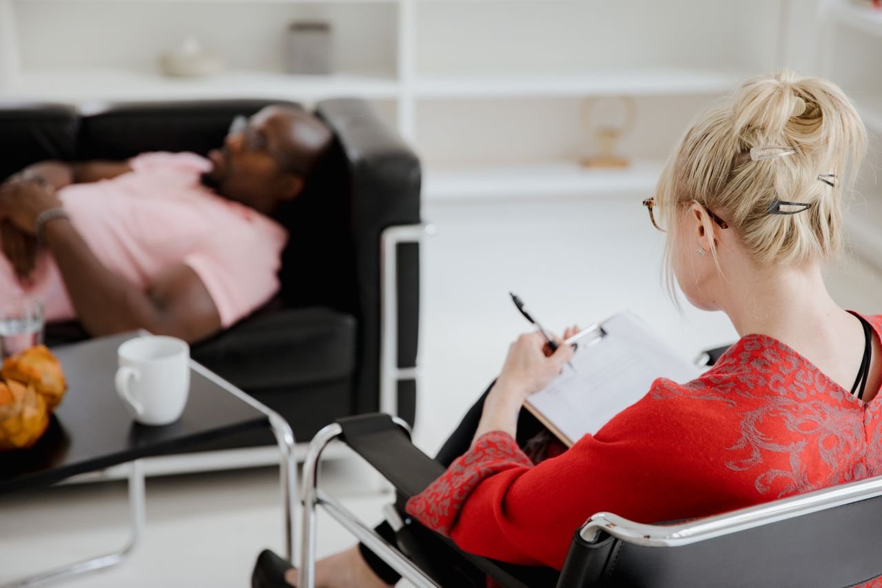 heros-img A professional therapist takes notes during a therapy session, engaging with a client.